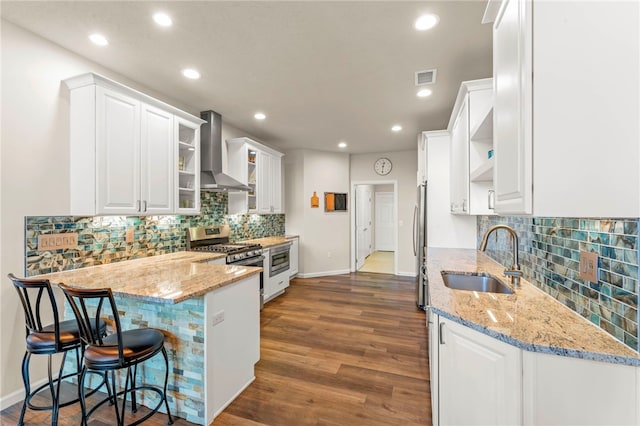 kitchen featuring a sink, stainless steel appliances, white cabinets, visible vents, and wall chimney range hood