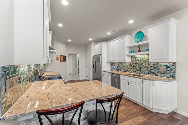 kitchen with a peninsula, a sink, stainless steel appliances, white cabinets, and decorative backsplash