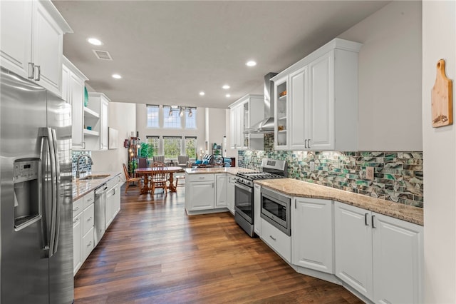 kitchen featuring a sink, a peninsula, wall chimney range hood, white cabinets, and appliances with stainless steel finishes