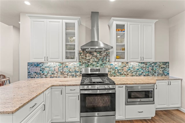 kitchen with light stone counters, light wood-type flooring, wall chimney exhaust hood, white cabinetry, and appliances with stainless steel finishes