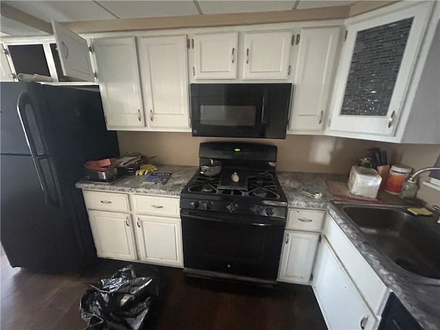 kitchen featuring a sink, black appliances, dark wood-style flooring, white cabinets, and light stone countertops