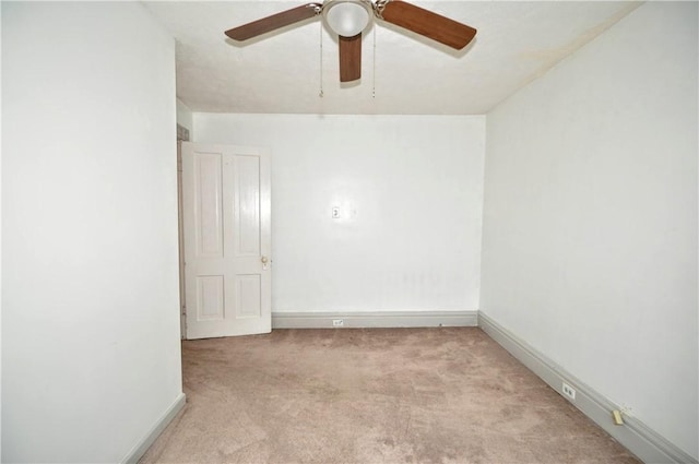 spare room featuring light colored carpet, a ceiling fan, and baseboards