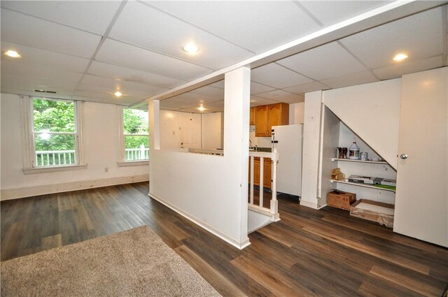 unfurnished living room with a drop ceiling, dark wood-type flooring, and baseboards