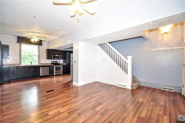unfurnished living room featuring ceiling fan, stairway, dark wood-style flooring, and a sink