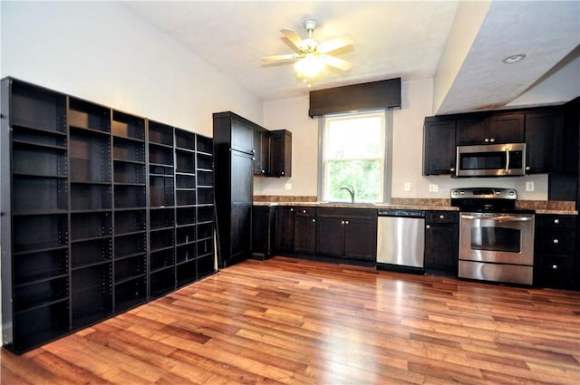 kitchen featuring appliances with stainless steel finishes, light wood finished floors, a ceiling fan, and a sink