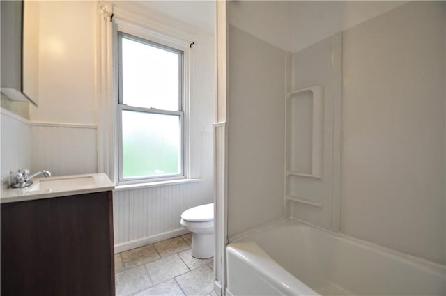 bathroom featuring toilet, vanity, a wainscoted wall, washtub / shower combination, and baseboards