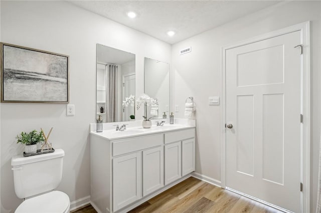 bathroom featuring double vanity, toilet, wood finished floors, a sink, and baseboards