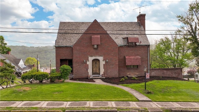 english style home with a front lawn, a chimney, and brick siding