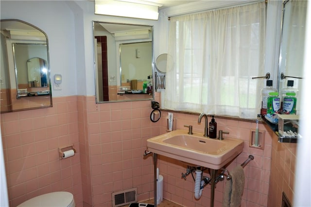 bathroom featuring tile walls, toilet, visible vents, and wainscoting