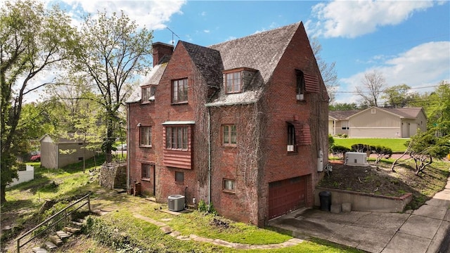 view of side of property with central air condition unit, driveway, brick siding, and a garage