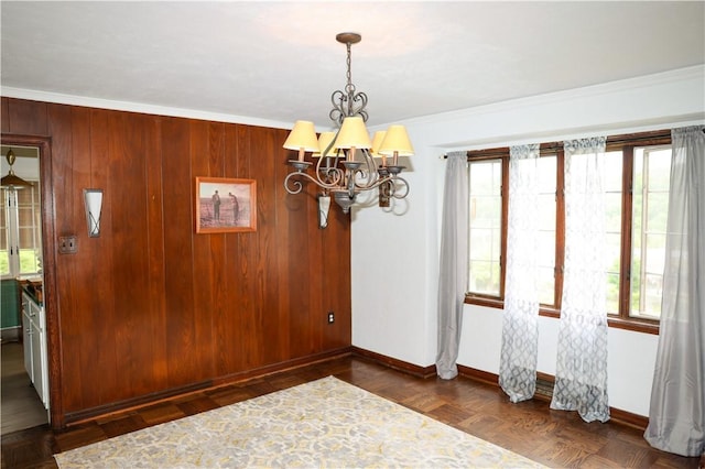 unfurnished dining area featuring a chandelier, wood walls, crown molding, and baseboards