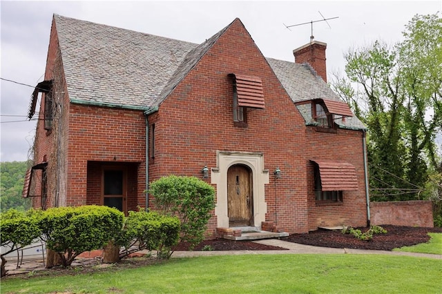 tudor house featuring a chimney, a high end roof, brick siding, and a front lawn