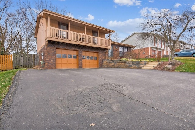 front of property featuring a garage, fence, a balcony, brick siding, and driveway