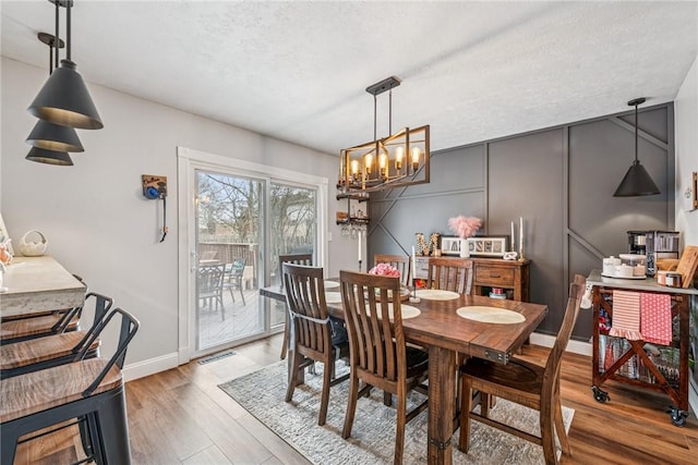 dining room with wood finished floors, a textured ceiling, visible vents, an inviting chandelier, and baseboards