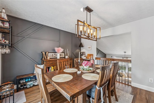 dining room with a decorative wall, a chandelier, baseboards, and wood finished floors