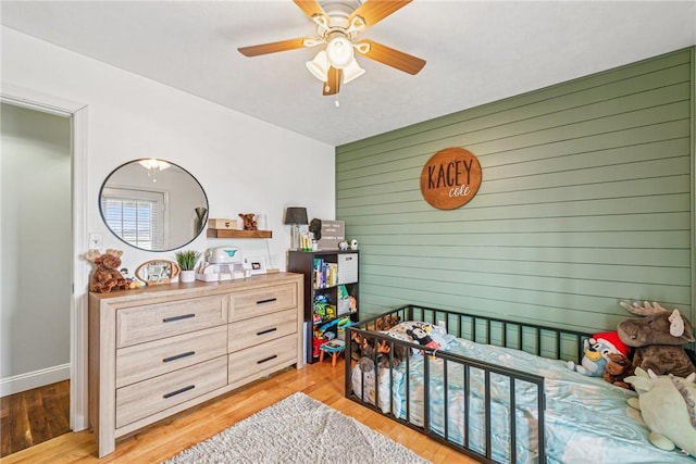 bedroom with baseboards, wooden walls, light wood-style flooring, and ceiling fan