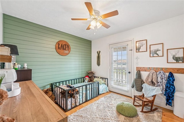 bedroom featuring ceiling fan, wood walls, access to outside, and wood finished floors