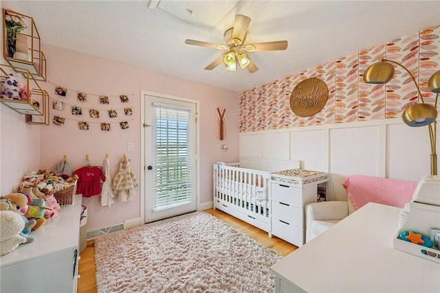 bedroom featuring wood finished floors, visible vents, a decorative wall, ceiling fan, and access to outside