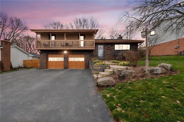 tri-level home with an attached garage, a chimney, aphalt driveway, a front lawn, and a balcony