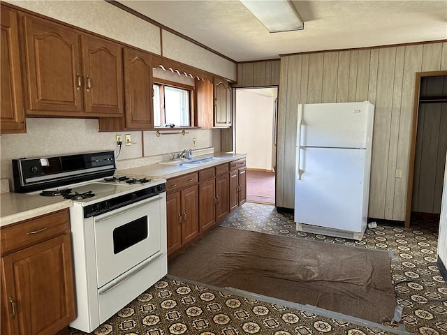 kitchen featuring white appliances, a sink, brown cabinets, light countertops, and dark floors