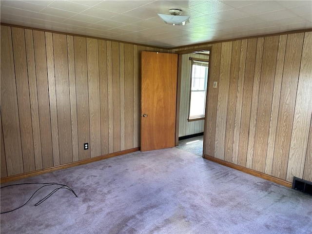 carpeted empty room featuring wood walls, baseboards, and visible vents