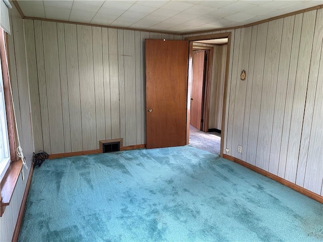 unfurnished room with baseboards, wooden walls, and carpet