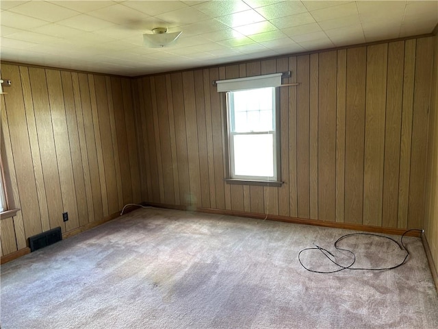 spare room featuring visible vents, wooden walls, and carpet floors