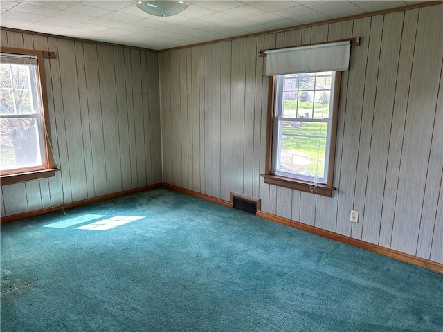 empty room featuring wooden walls, plenty of natural light, carpet floors, and visible vents