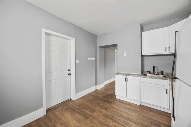 interior space featuring a sink, freestanding refrigerator, dark wood finished floors, white cabinets, and baseboards