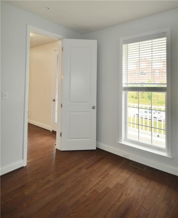unfurnished room with a wealth of natural light, baseboards, and dark wood-type flooring