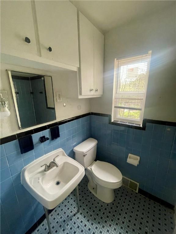 bathroom with a sink, tile walls, a wainscoted wall, and visible vents