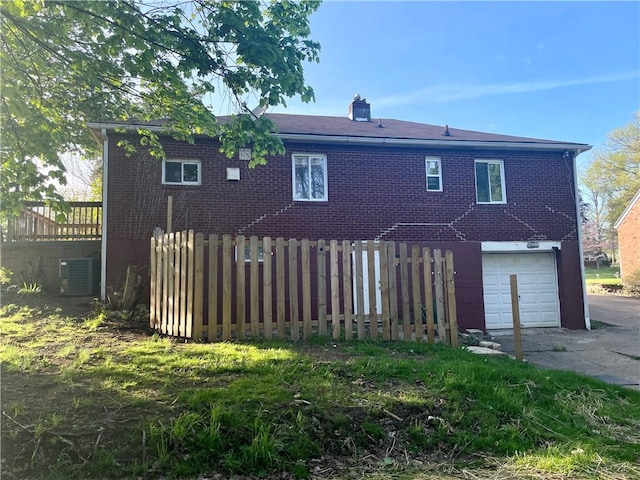 back of house with an attached garage, brick siding, central AC unit, and fence