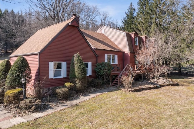 exterior space with a chimney, a deck, a shingled roof, and a lawn
