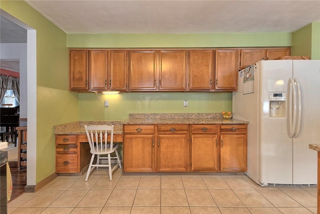 kitchen featuring brown cabinetry, light tile patterned floors, white refrigerator with ice dispenser, and built in study area