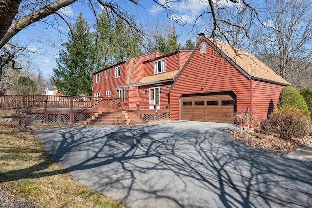 rustic home featuring a garage, a chimney, a deck, roof with shingles, and driveway