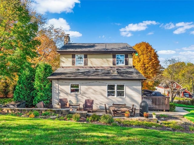 rear view of property featuring a chimney, a deck, a patio area, and a lawn
