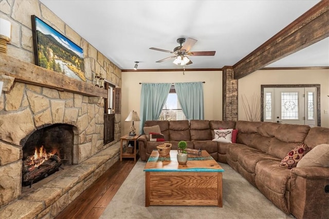 living room featuring ceiling fan, a stone fireplace, crown molding, and wood finished floors