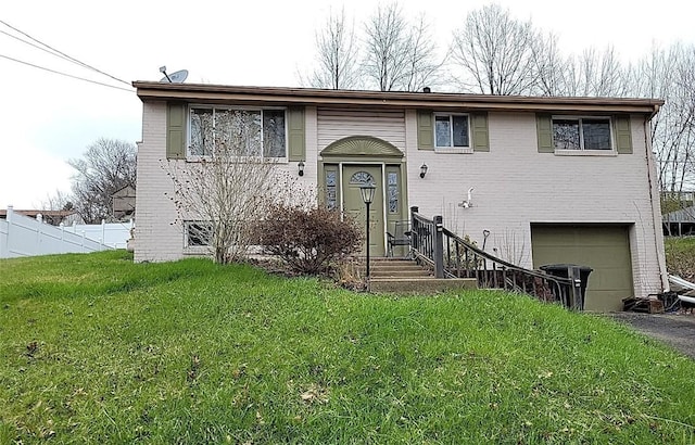 raised ranch featuring brick siding, fence, an attached garage, a front yard, and aphalt driveway