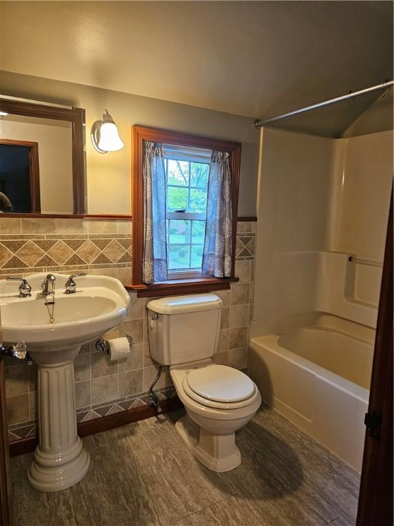 full bathroom featuring toilet, tile walls, shower / bathtub combination, and a wainscoted wall