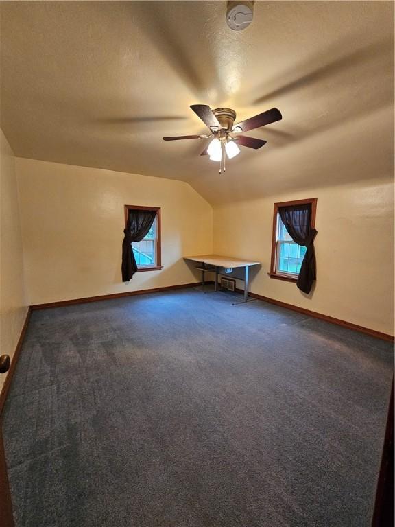 bonus room featuring vaulted ceiling, dark colored carpet, and baseboards