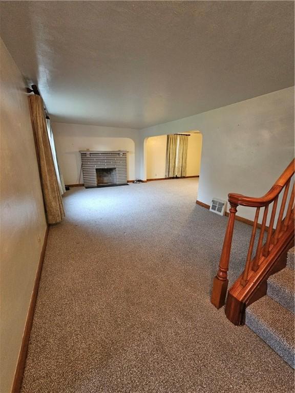 carpeted living area with stairway, a fireplace, baseboards, and arched walkways