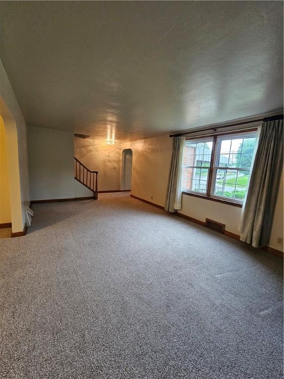 unfurnished living room featuring carpet, baseboards, and arched walkways