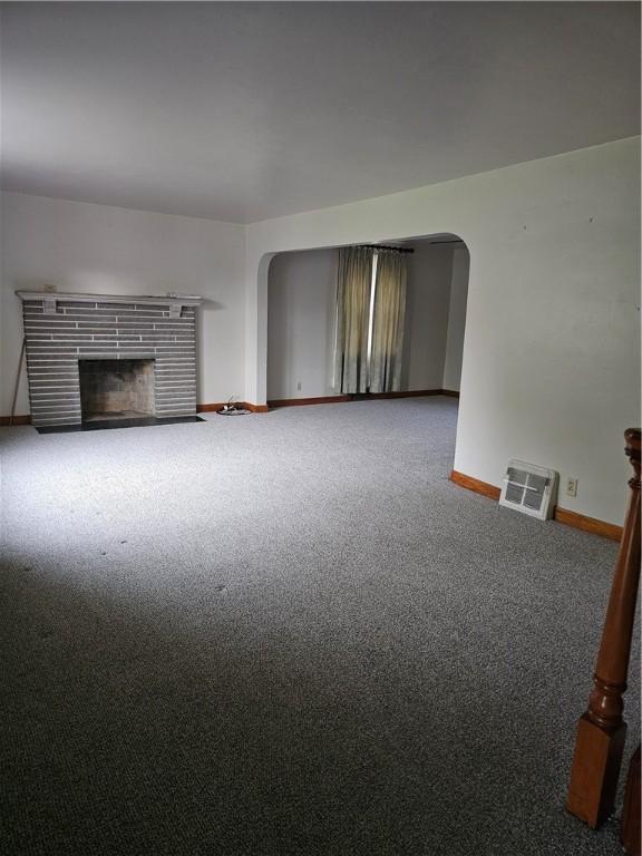 unfurnished living room featuring arched walkways, carpet flooring, a fireplace, and baseboards