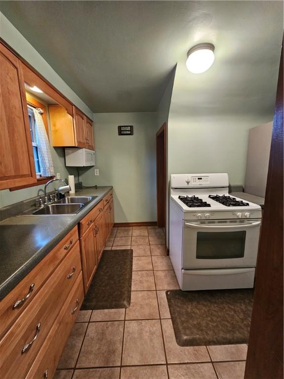 kitchen featuring brown cabinetry, white appliances, light tile patterned flooring, and a sink