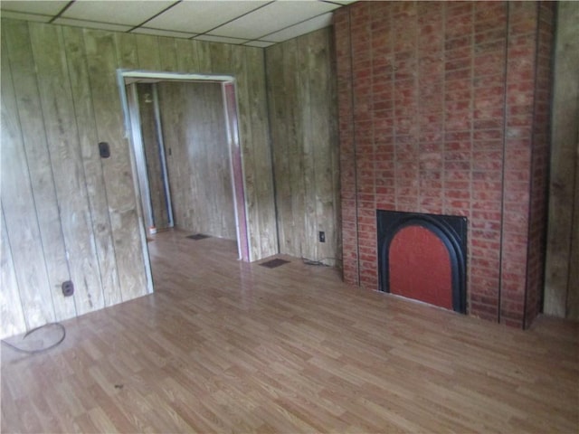 unfurnished living room featuring a drop ceiling, wood walls, a brick fireplace, and wood finished floors