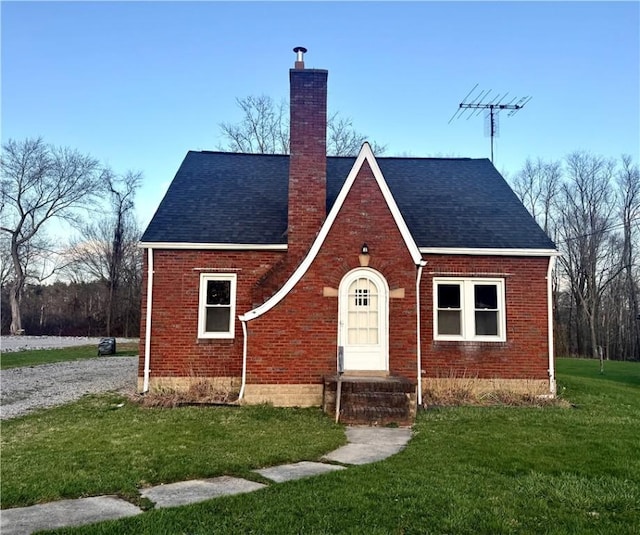 tudor-style house with a front lawn, a shingled roof, brick siding, and a chimney