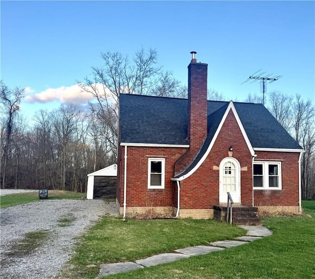 english style home with a chimney, a front yard, roof with shingles, and brick siding
