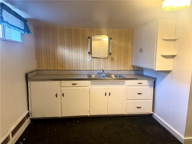 kitchen featuring white cabinets, wallpapered walls, and a sink