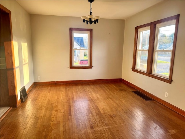 empty room featuring baseboards, an inviting chandelier, visible vents, and wood finished floors