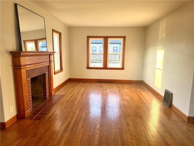 unfurnished living room featuring baseboards, a tiled fireplace, visible vents, and wood finished floors